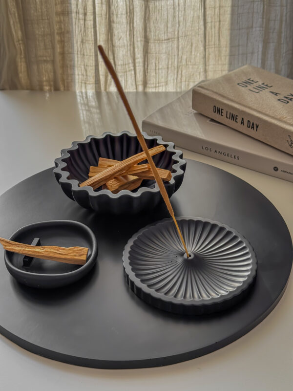 black scalloped bowl standing on round black big tray together with palo santo and incense holder